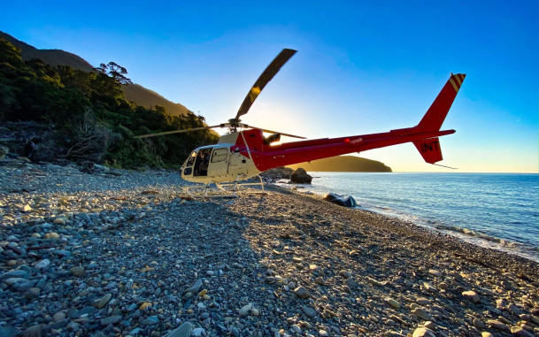 Helicopter parked on a rocky beach with the shoreline visible.