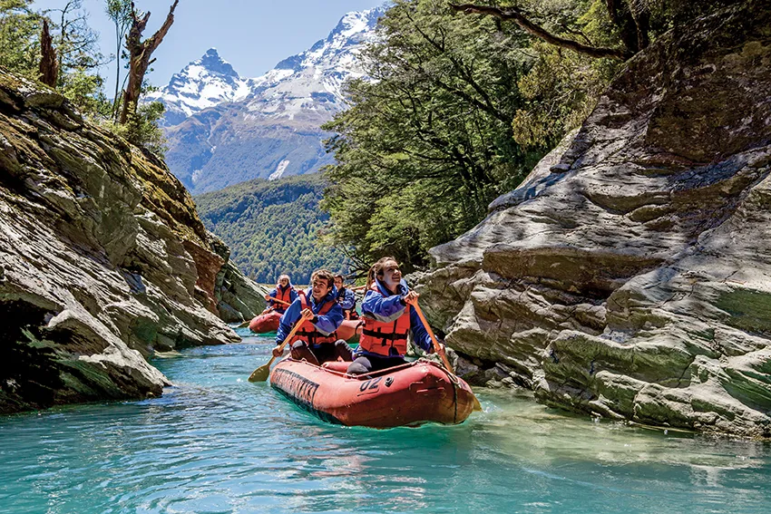 Girl paddling inflatable kayak through narrow rocky waterway 