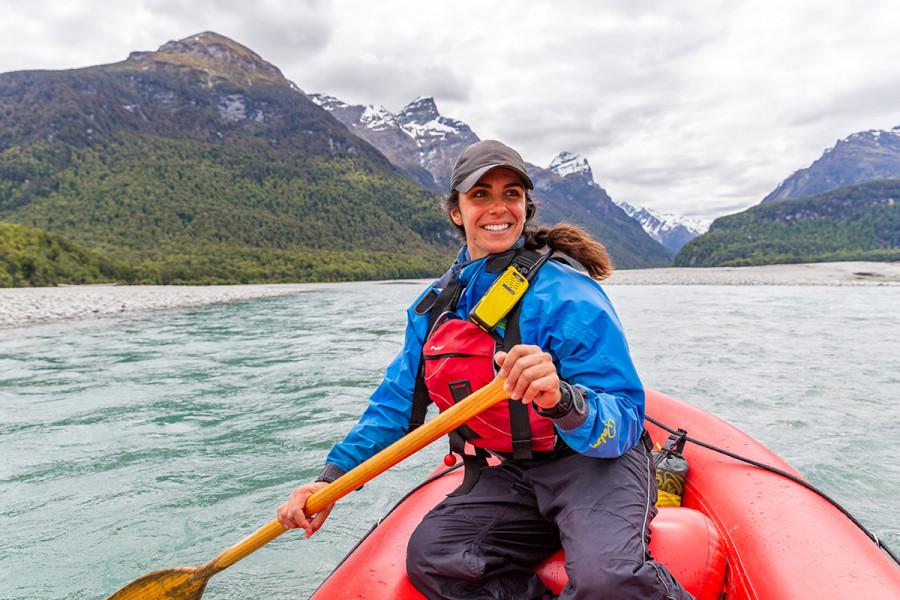 Smiling woman wearing lifejacket paddling kayak downstream 