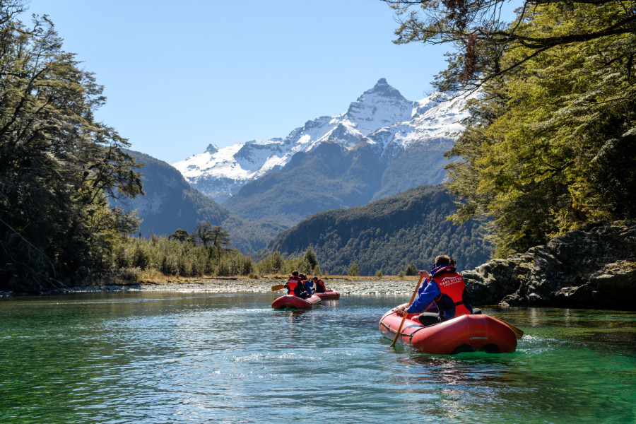 Two kayaks paddling towards snowcapped mountain range