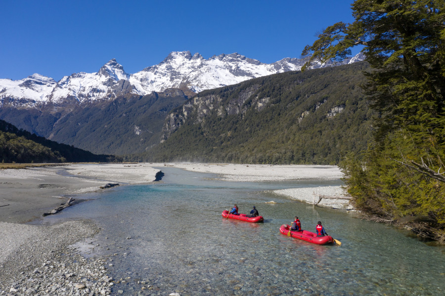two kayaks paddling down river towards alpine mountain range