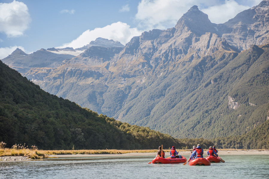 Group of four kayaks in river paddling towards mountain range in distance