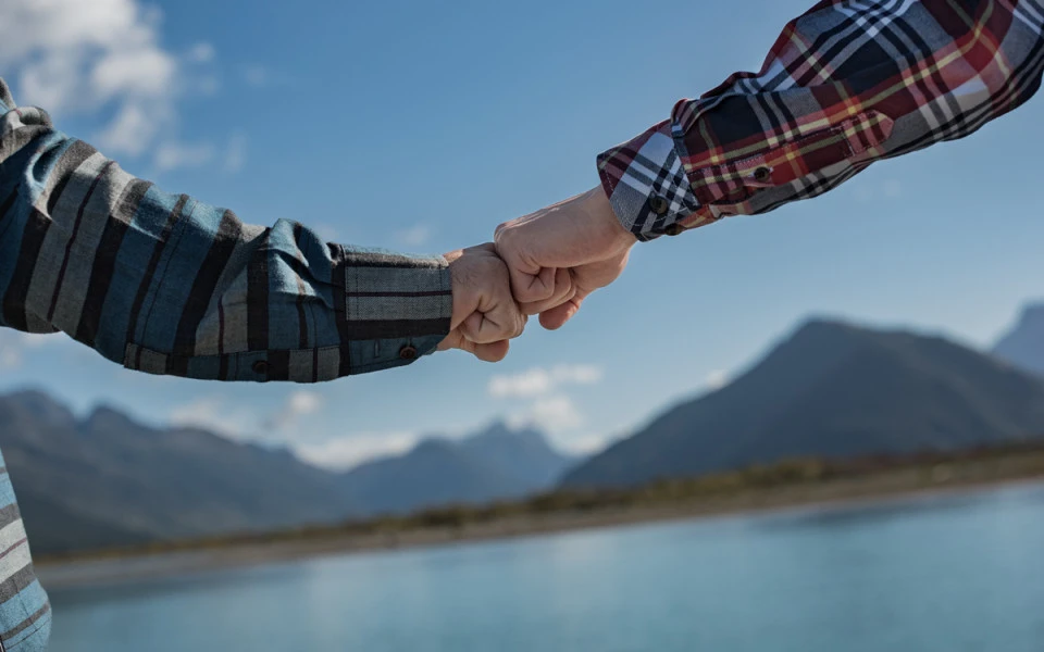Two hands touching knuckles with Dart River and mountains in the background