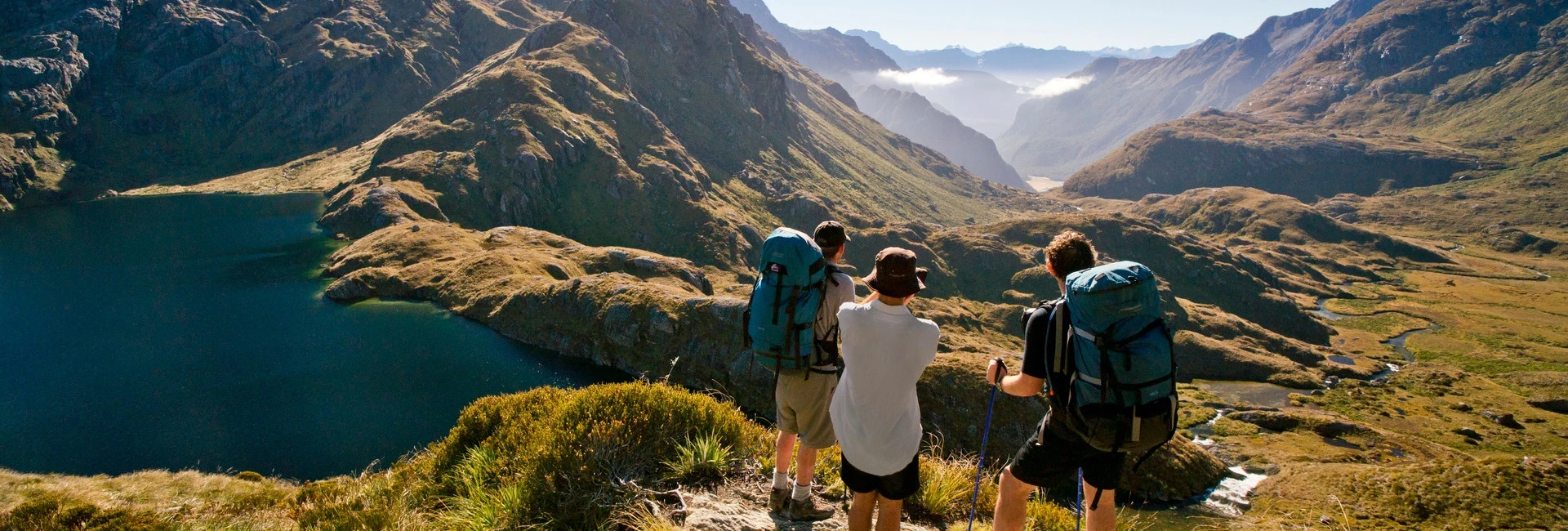 Group of hikers wearing backpacks on the Routeburn Track, standing at a lookout with expansive mountain views.
