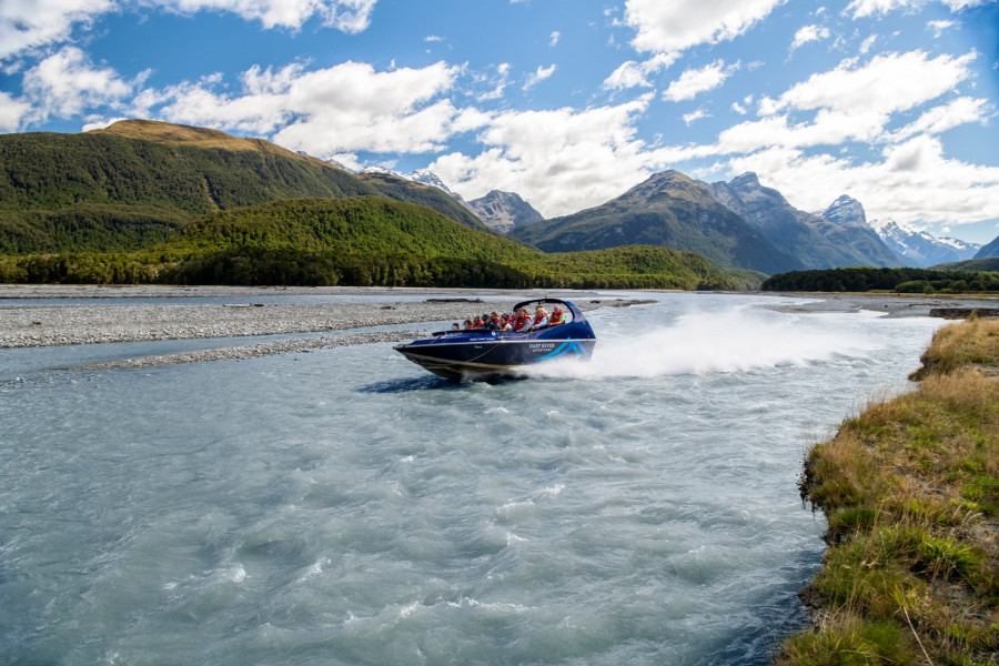 Jet boat racing up river with alpine view behind