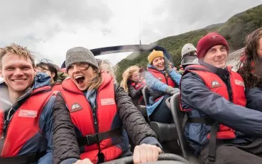 Close-up of visitors on a jet boat as it speeds down the river, with excited, smiling faces.