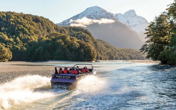 Visitors on board the Wilderness Jet boat on the Dart River, surrounded by native trees and towering mountains