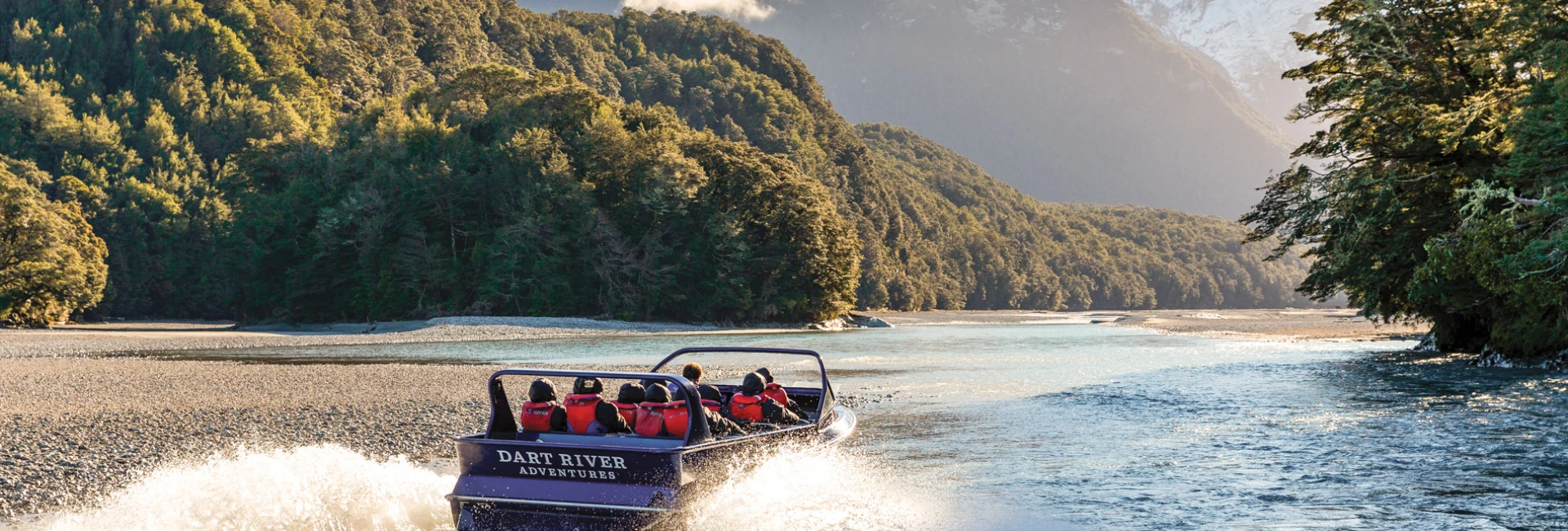 Visitors on board the Wilderness Jet boat on the Dart River, surrounded by native trees and towering mountains