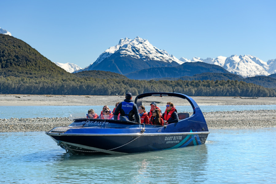 Guide talking to passengers on a Wilderness Jet boat on the Dart River with mountains in the background