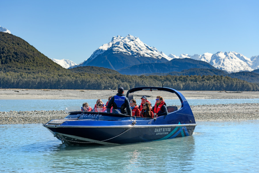 Jet boat driver standing aboard talking to passengers with snowcapped mountains in background